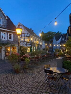 A cobblestone courtyard with outdoor seating and string lights, surrounded by traditional European buildings. - 1-Bedroom Apartment in Solingen (Solingen)