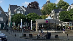 En kullerstensgata med historiska byggnader, ett kyrktorn och ett överbyggt marknadsområde.