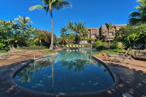 A pool with lounge chairs, palm trees, and a building in the background.