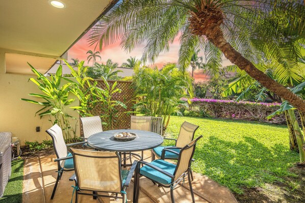 A patio with a round table and chairs, surrounded by lush greenery and a palm tree.