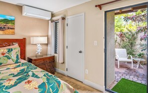 A bedroom with a bed, bedside table, lamp, and a view of an outdoor patio with chairs and plants.