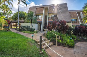 A modern hotel with a two-story structure, a central staircase, and a well-maintained garden with tropical plants.