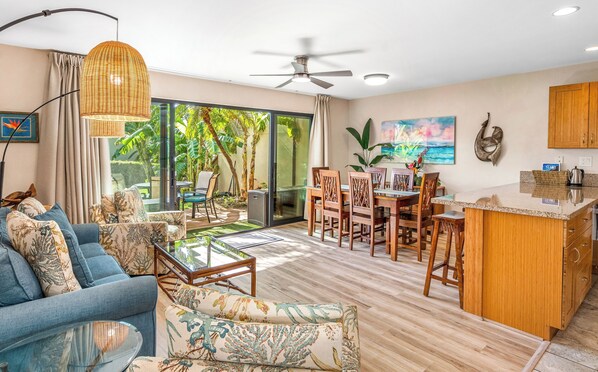 A spacious living area with a sofa, chairs, a dining table, and a kitchen area with wooden cabinets and a countertop.