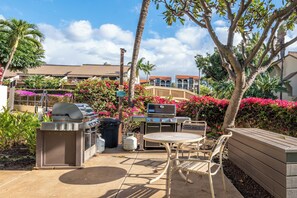An outdoor patio with a grill, table, chairs, and a trash can.