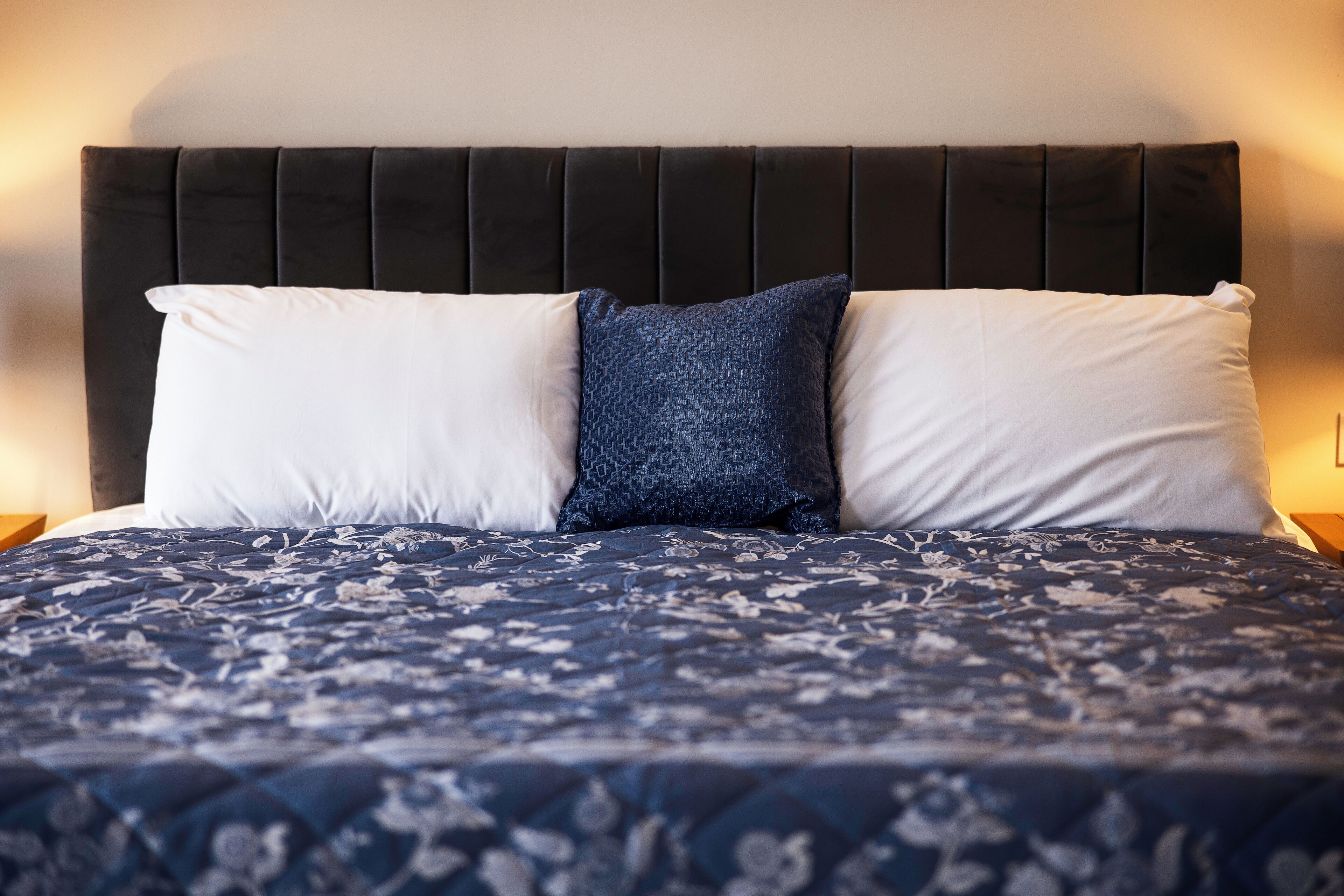 Uma cama com cabeceira escura e roupa de cama com padrão floral.
