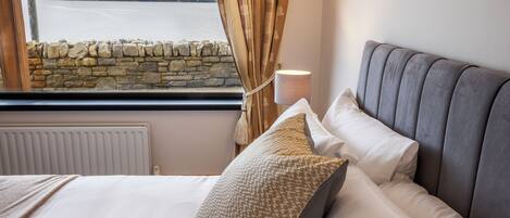 A bedroom with a bed, a stone wall, a window with curtains, and a lamp.