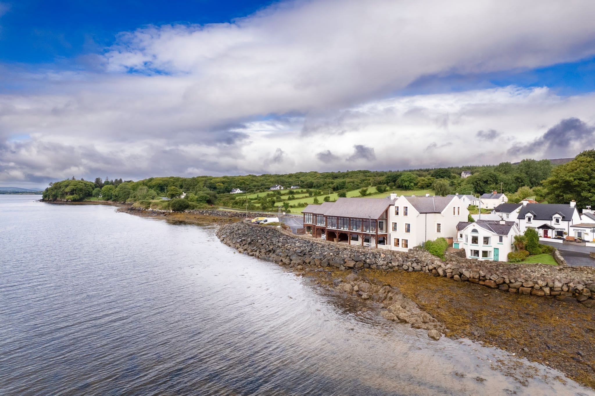 A coastal town with houses along the shore, a stone wall, and a clear view of the sea.