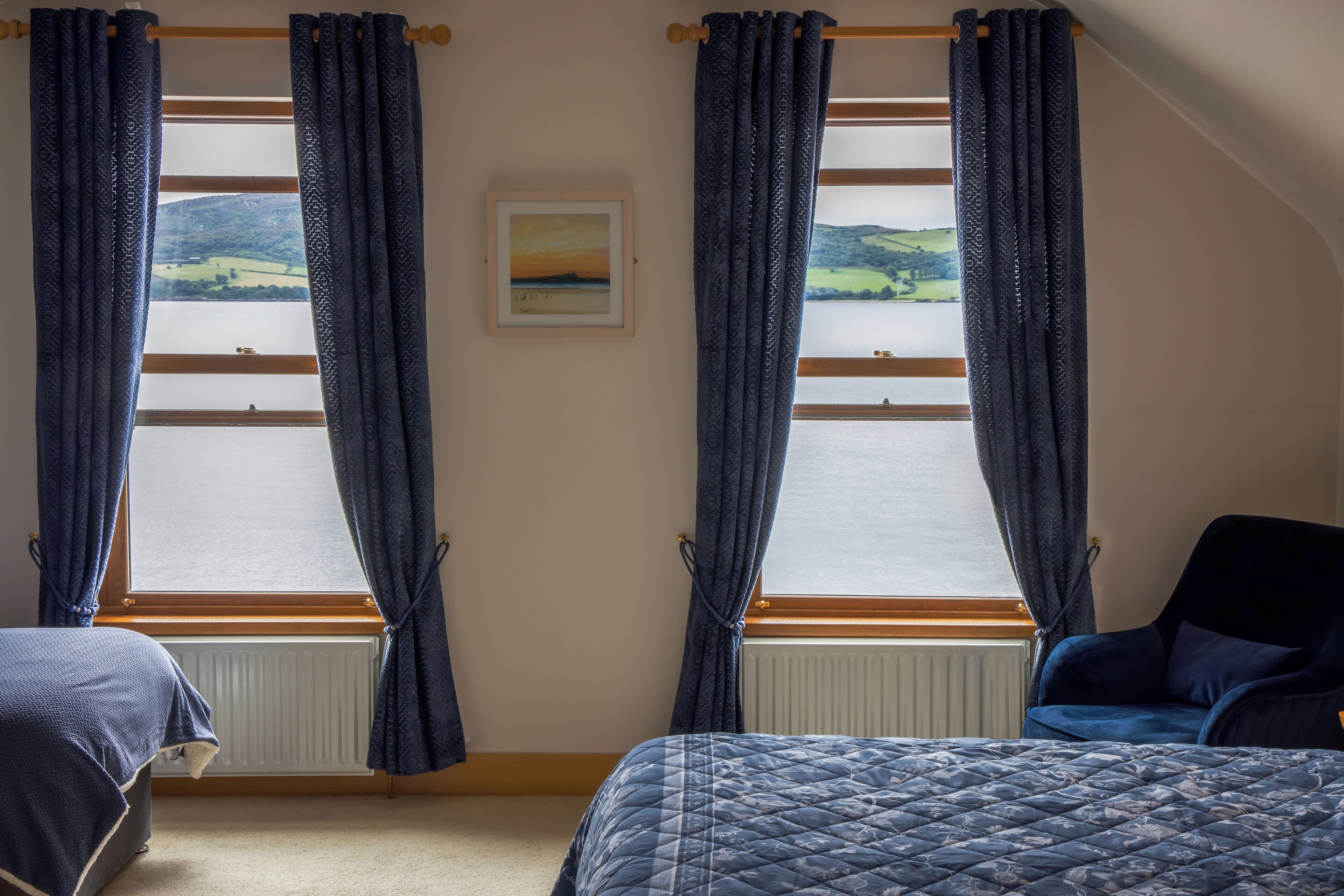 Un dormitorio con dos camas, vista al mar a través de amplios ventanales y un cuadro enmarcado en la pared.
