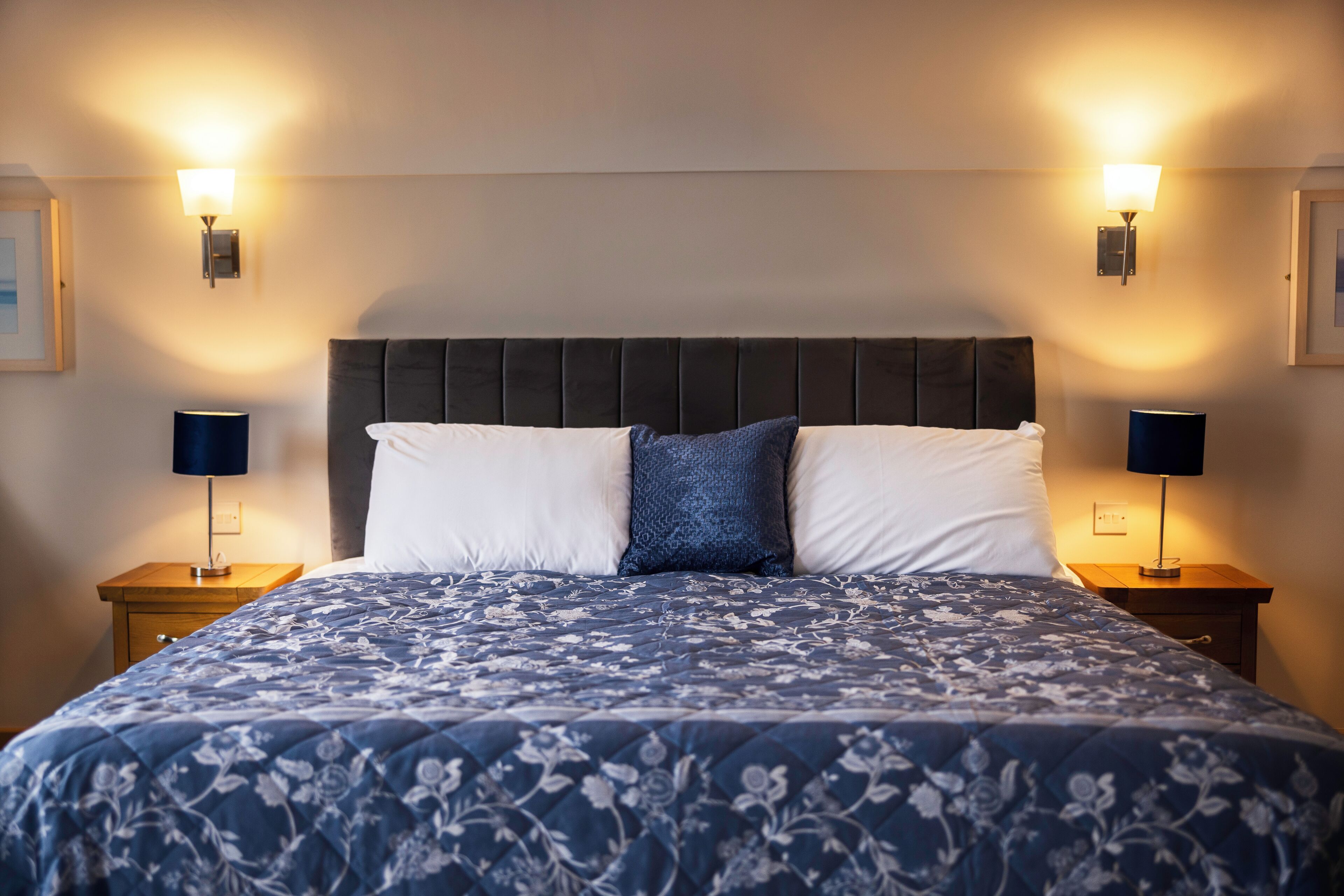 A neatly made bed with a floral-patterned bedspread, two bedside lamps, and a dark headboard.