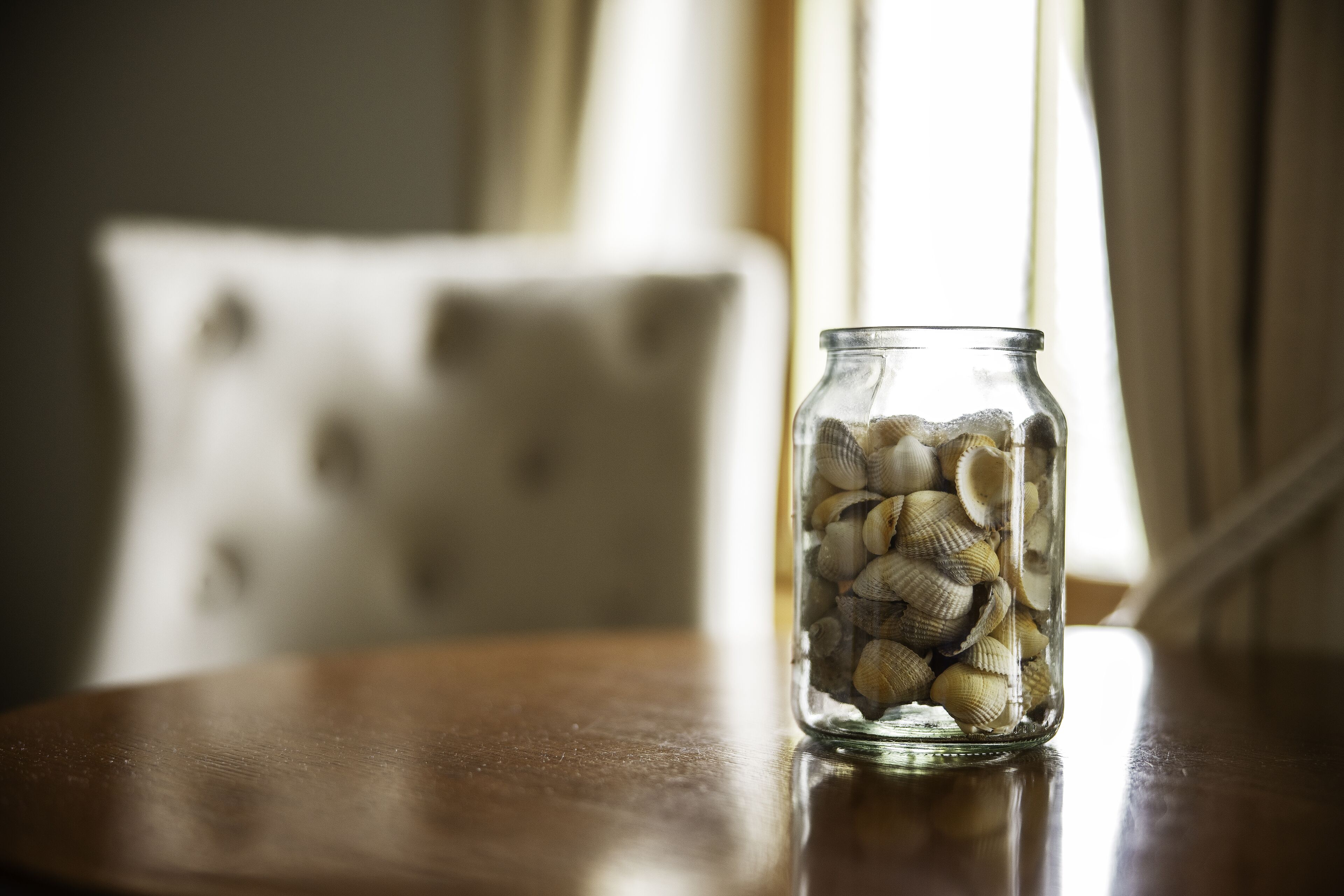 A glass jar filled with seashells on a wooden table.