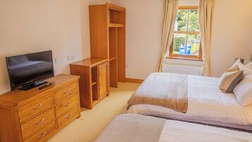 A bedroom with a TV on a wooden dresser, a wardrobe, a bed with pillows, and a window with curtains.