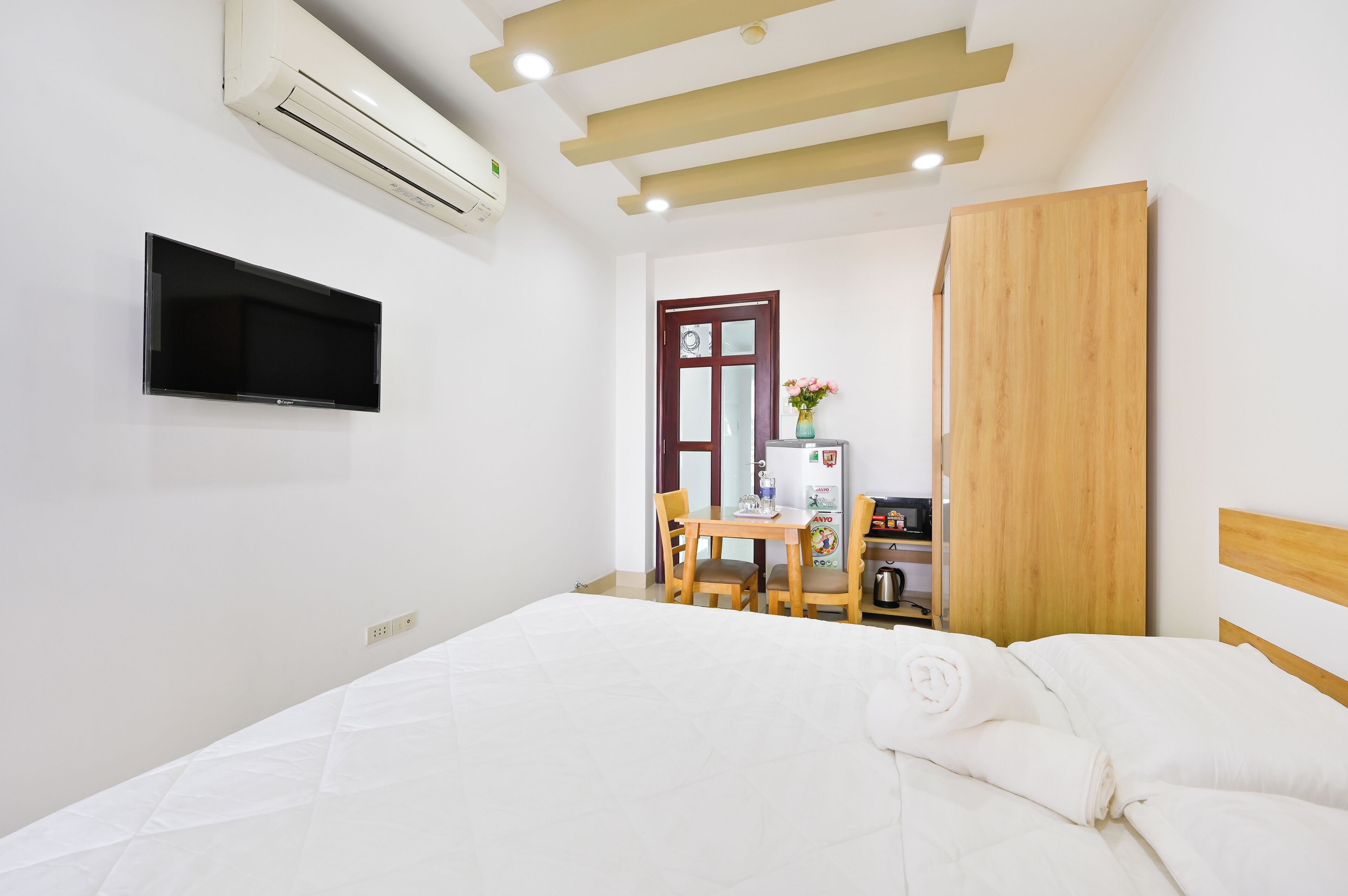 A hotel room with a bed, a desk with a chair, a TV mounted on the wall, and an air conditioning unit.