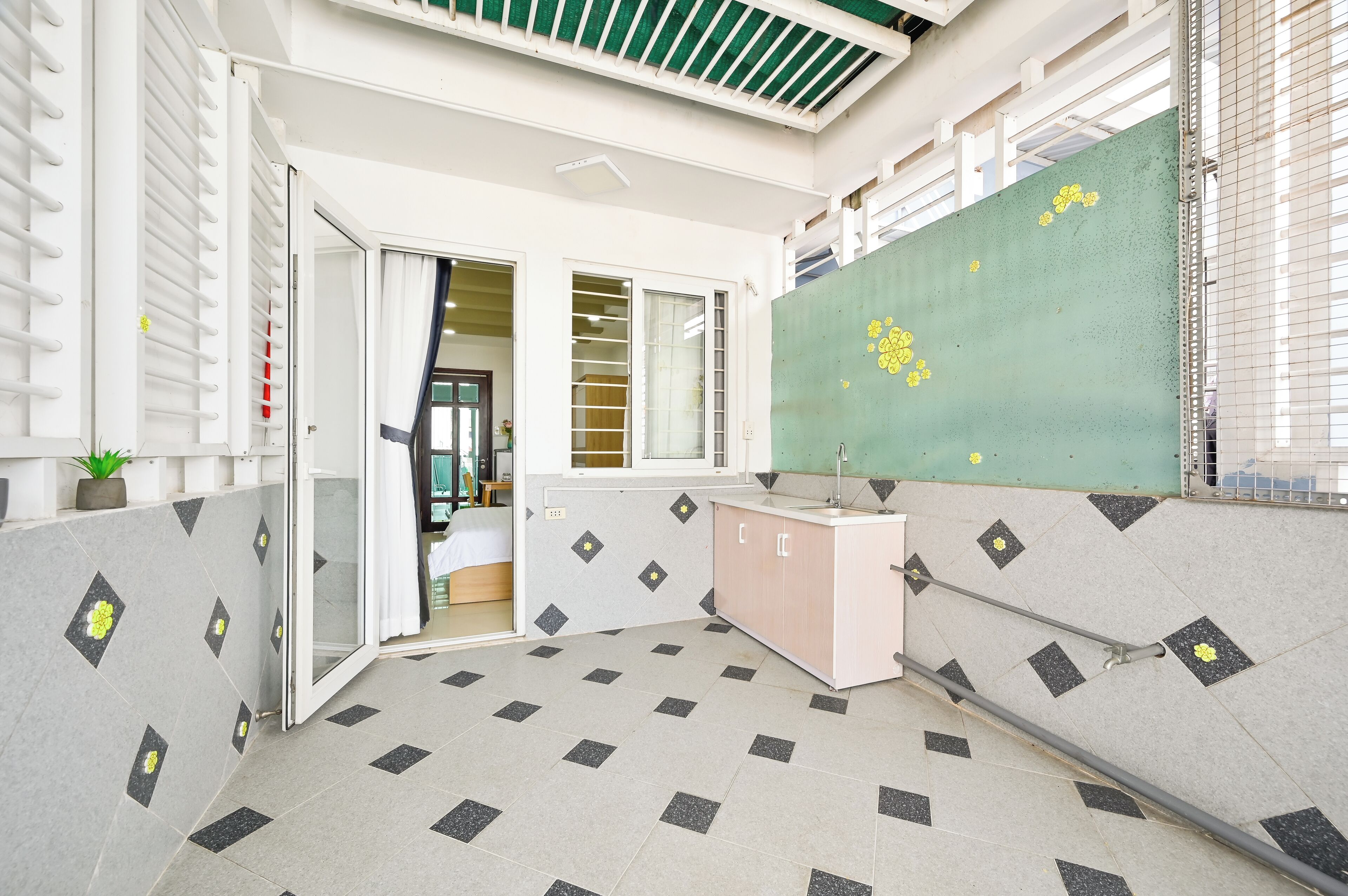 A modern hotel lobby with a tiled floor, a green wall with yellow floral decals, a pink reception desk, and a staircase leading to an upper level.