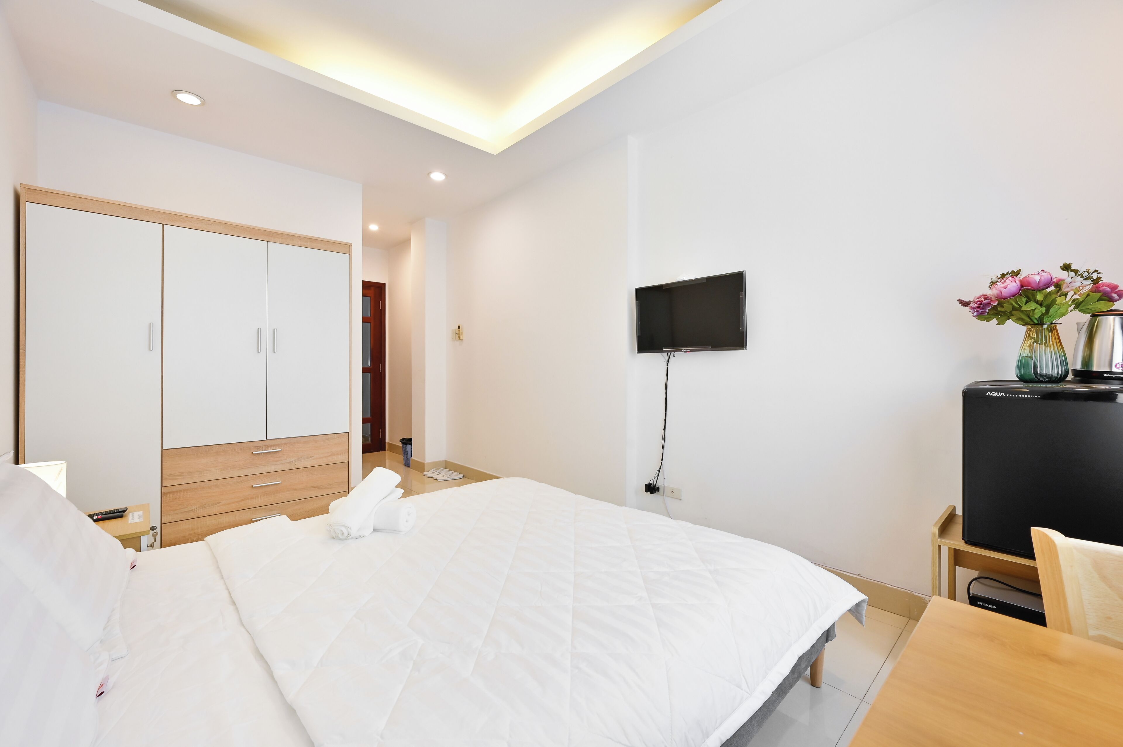 A hotel room with a large bed, a wooden wardrobe, a flat-screen TV, and a small table with a vase of flowers.