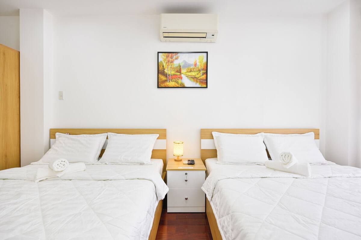 Et hotelværelse med to senge, et natbord med lampe, en vægmonteret aircondition og et indrammet billede over sengene.