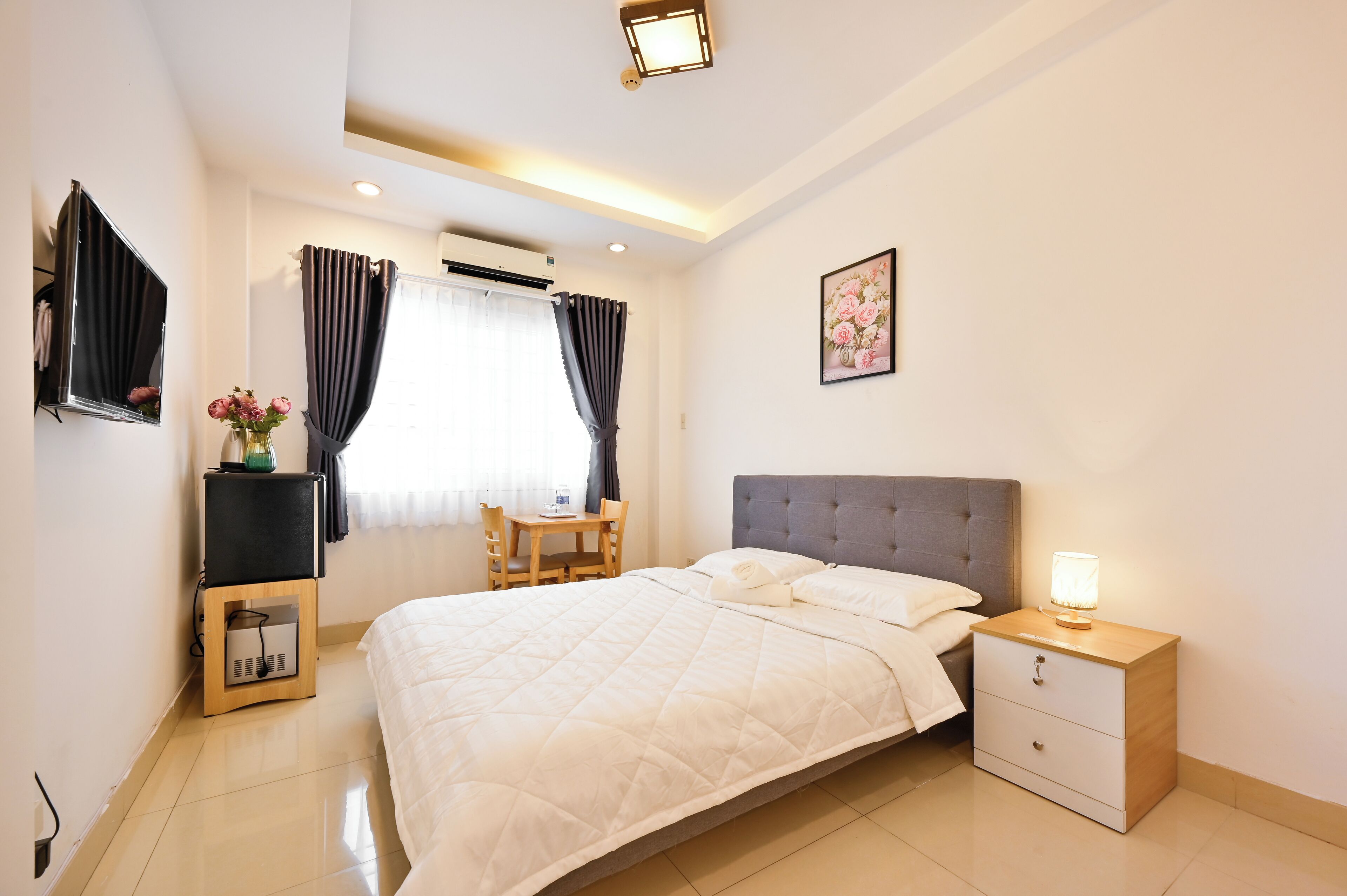 A neatly arranged bedroom with a large bed, bedside table, and a small desk with a chair.