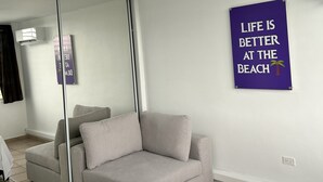 Un dormitorio con una cama, un sofá gris, un ventilador de techo, un espejo grande y un cartel motivacional.