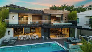 Une maison moderne à plusieurs étages, dotée d’une piscine sur le toit, d’un espace extérieur aménagé et d’un intérieur spacieux avec une cheminée.