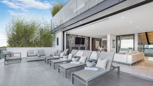 Un espace de vie extérieur moderne, doté de nombreux coins salon, notamment des canapés et des fauteuils, aménagé sur une vaste terrasse.