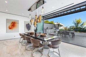 Une cuisine moderne dotée d’un grand îlot central, de luminaires suspendus et offrant une vue sur l’extérieur.