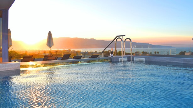 Piscina con vista a las montañas al atardecer, sillas de descanso y zona junto a la piscina.