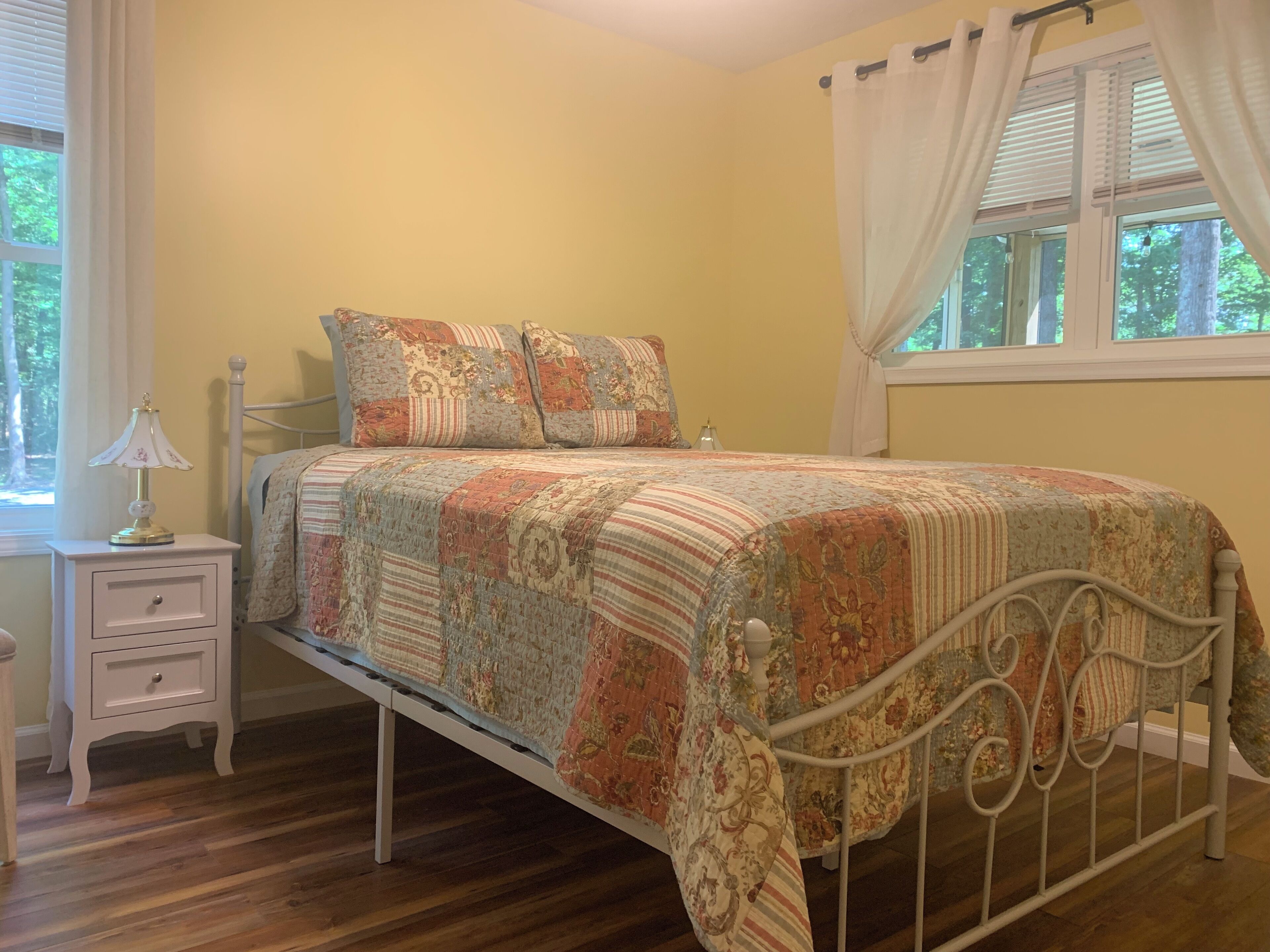 Un dormitorio con cama, mesita de noche, lámpara y ventana con cortinas.