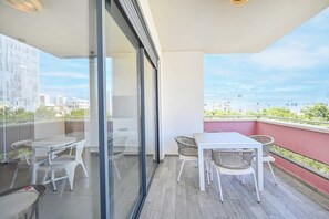 A balcony with a glass door, a white table, and wicker chairs. - Cozy 2BR with Balcony and Mamad on Dizzengoff by HolyGuest (Tel Aviv-Yafo)