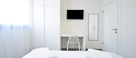 Une chambre d’hôtel comprenant un lit, un téléviseur fixé au mur, un bureau avec une chaise et une armoire.