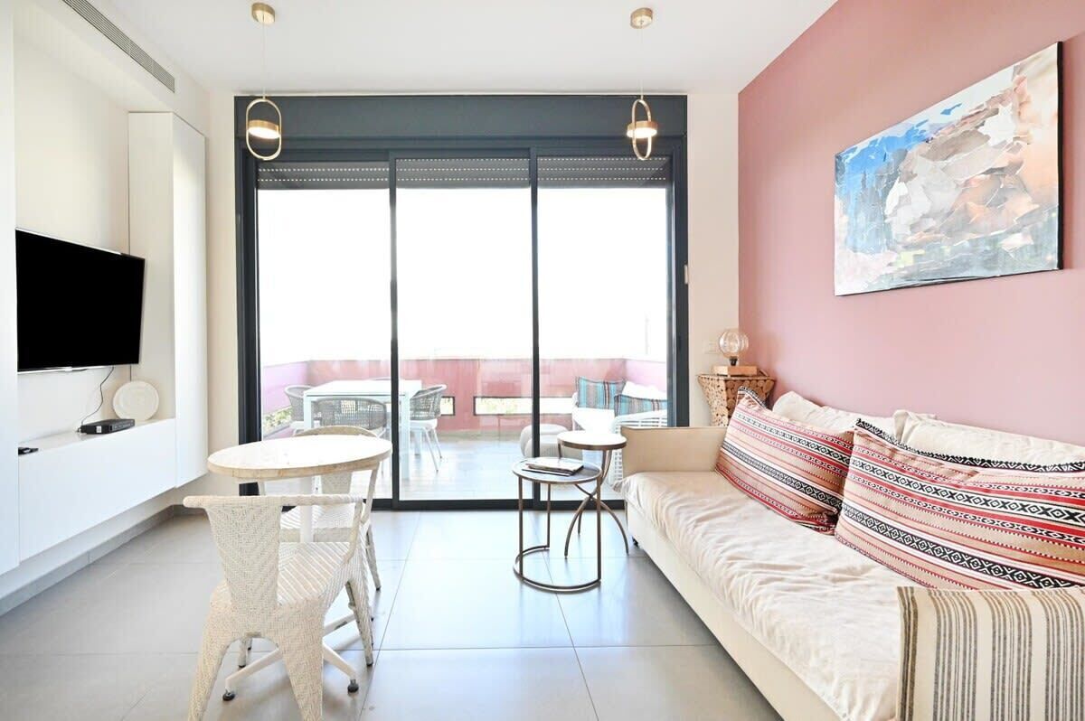 A modern living room with a sofa, a television, and a balcony with outdoor furniture.