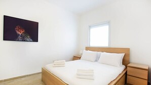 Un dormitorio moderno con una cama de madera, ropa de cama blanca, una mesita de noche y un cuadro en la pared.