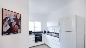 Una cocina moderna con armarios blancos, horno empotrado, lavamanos y refrigerador.