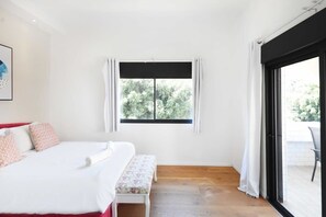 A bedroom with a bed, a bench, a window, and a sliding glass door leading to an outdoor area.