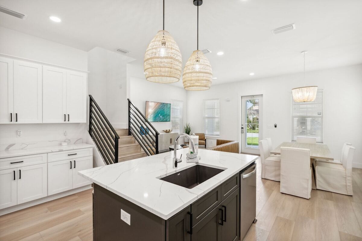 A modern kitchen with white cabinets, a marble island, and pendant lighting.