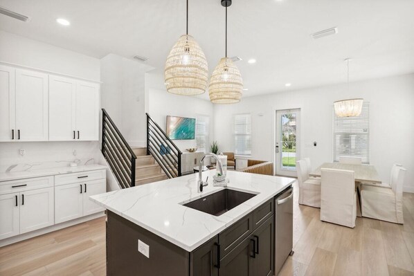 A modern kitchen with white cabinets, a marble island, and pendant lighting.