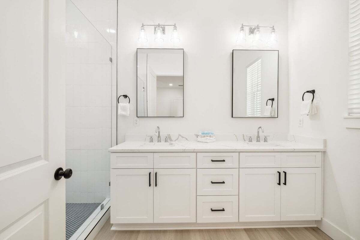 A modern bathroom with a double vanity, two mirrors, and a shower area.