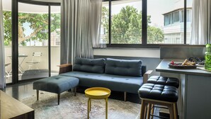 Una sala de estar moderna con un sofá gris, un taburete amarillo y una zona de comedor con una pequeña mesa y sillas.