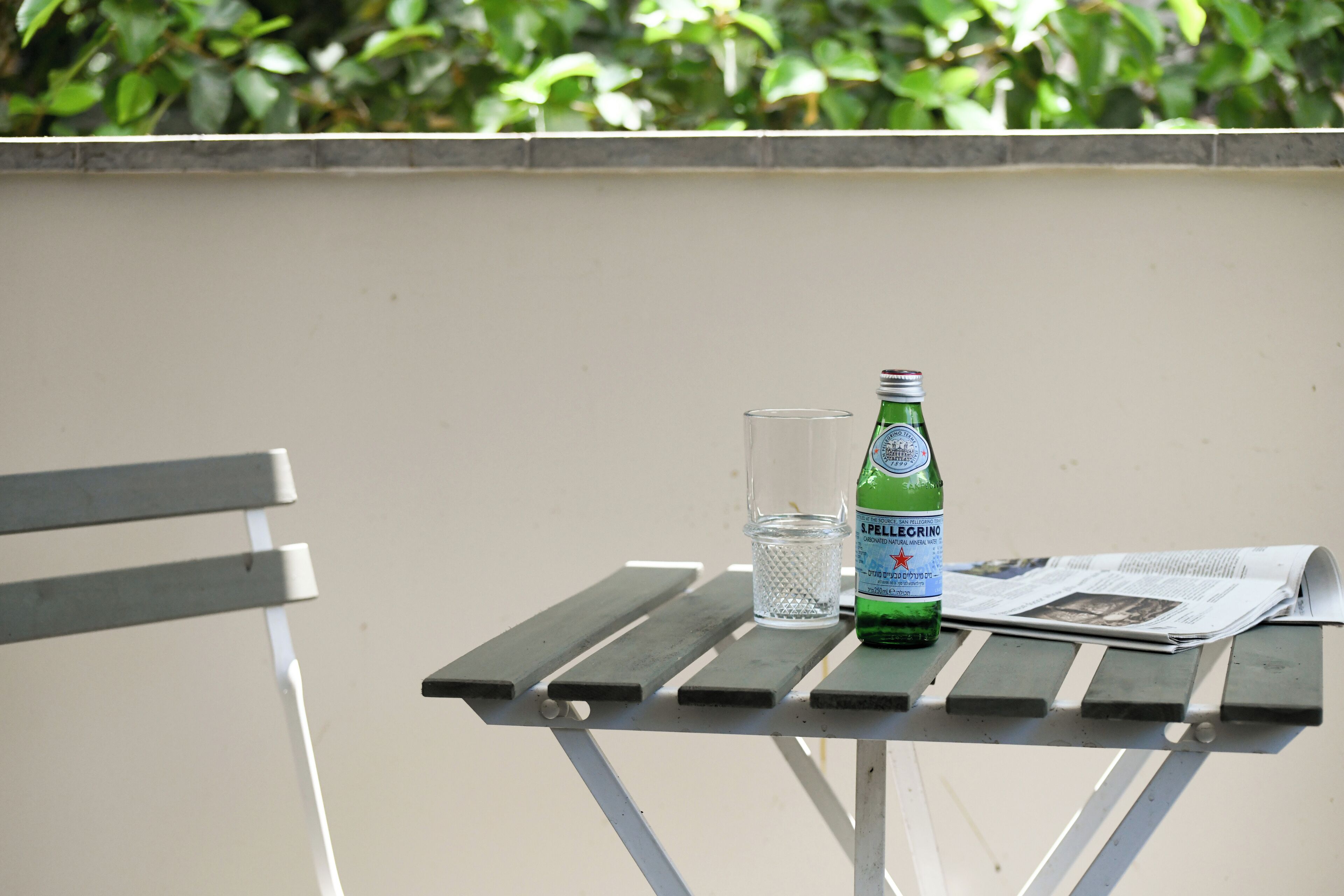 A table with a bottle, a glass, and a newspaper.