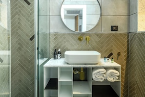A modern bathroom with a glass shower enclosure, a white sink with a marble countertop, and a herringbone-patterned tile backsplash.
