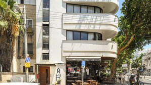 Un edificio de varios pisos con fachada curva, zona de estar al aire libre y una entrada visible.