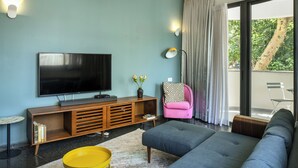 Una sala de estar moderna con un televisor de pantalla plana, un mueble de madera para entretenimiento, un sofá, un taburete amarillo y una silla rosa.