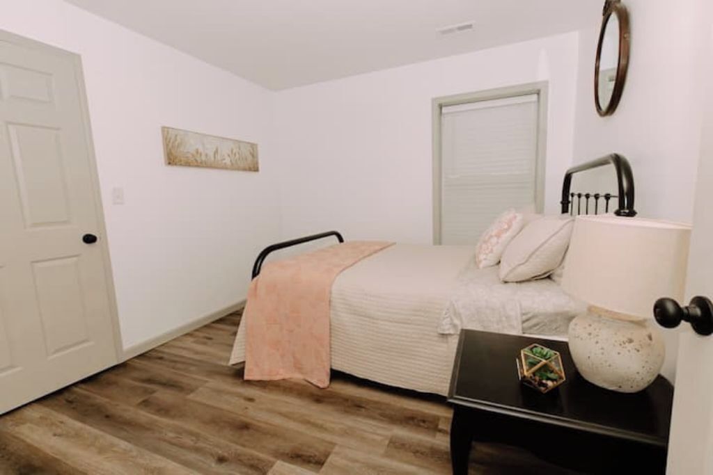 A bedroom with a bed, a nightstand, a door, and a wall-mounted mirror.