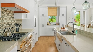 Una cocina moderna con armarios blancos, estufa a gas y un amplio ventanal con vistas al verdor.