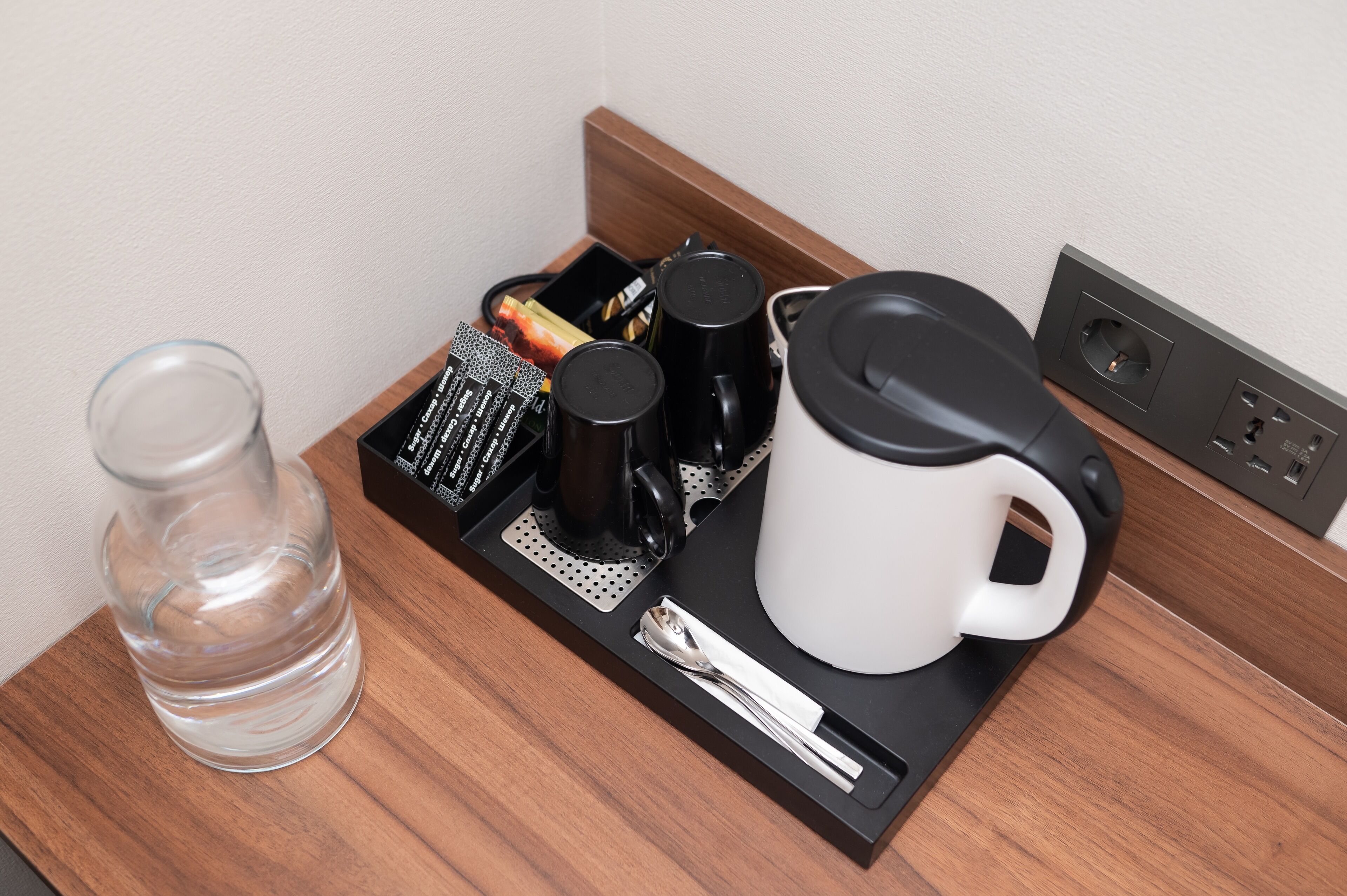 Bandeja de café da manhã em quarto de hotel, com um copo de água, máquina de café, caneca e colher.