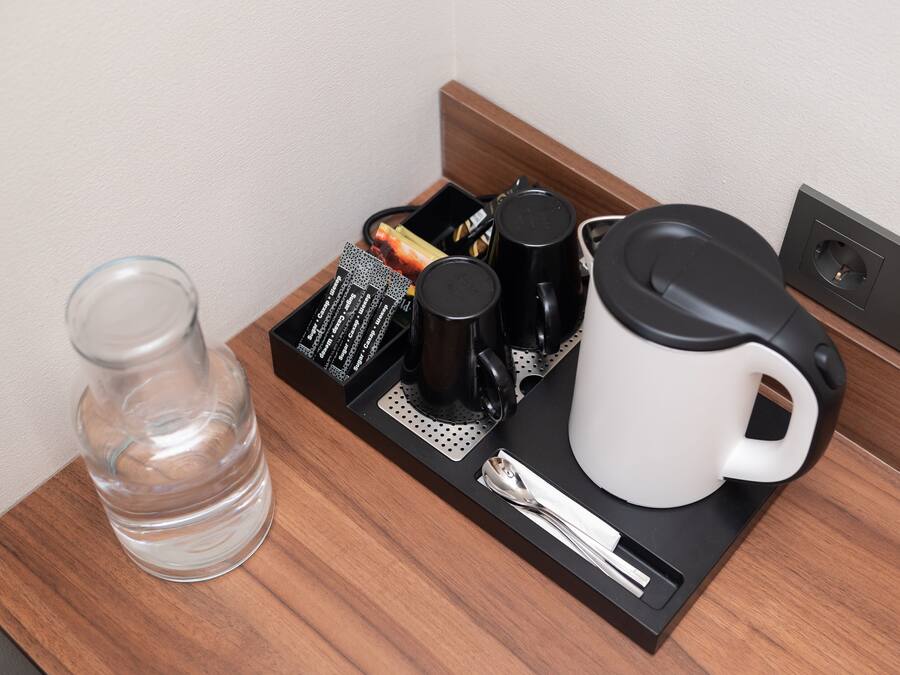 Bandeja de café da manhã em quarto de hotel, com um copo de água, máquina de café, caneca e colher.