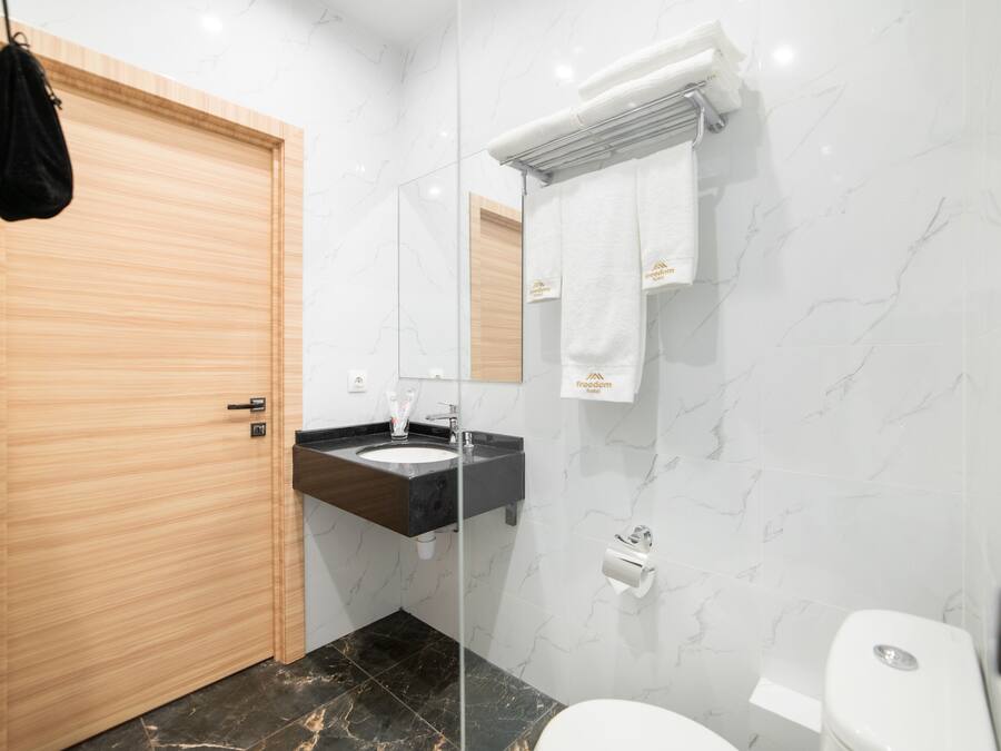 A modern bathroom with a wooden door, a black countertop sink, a white toilet, and a mirror with a towel hanging on it.