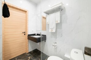Un baño moderno con puerta de madera, un lavamanos con encimera negra, inodoro blanco y un espejo con una toalla colgada.