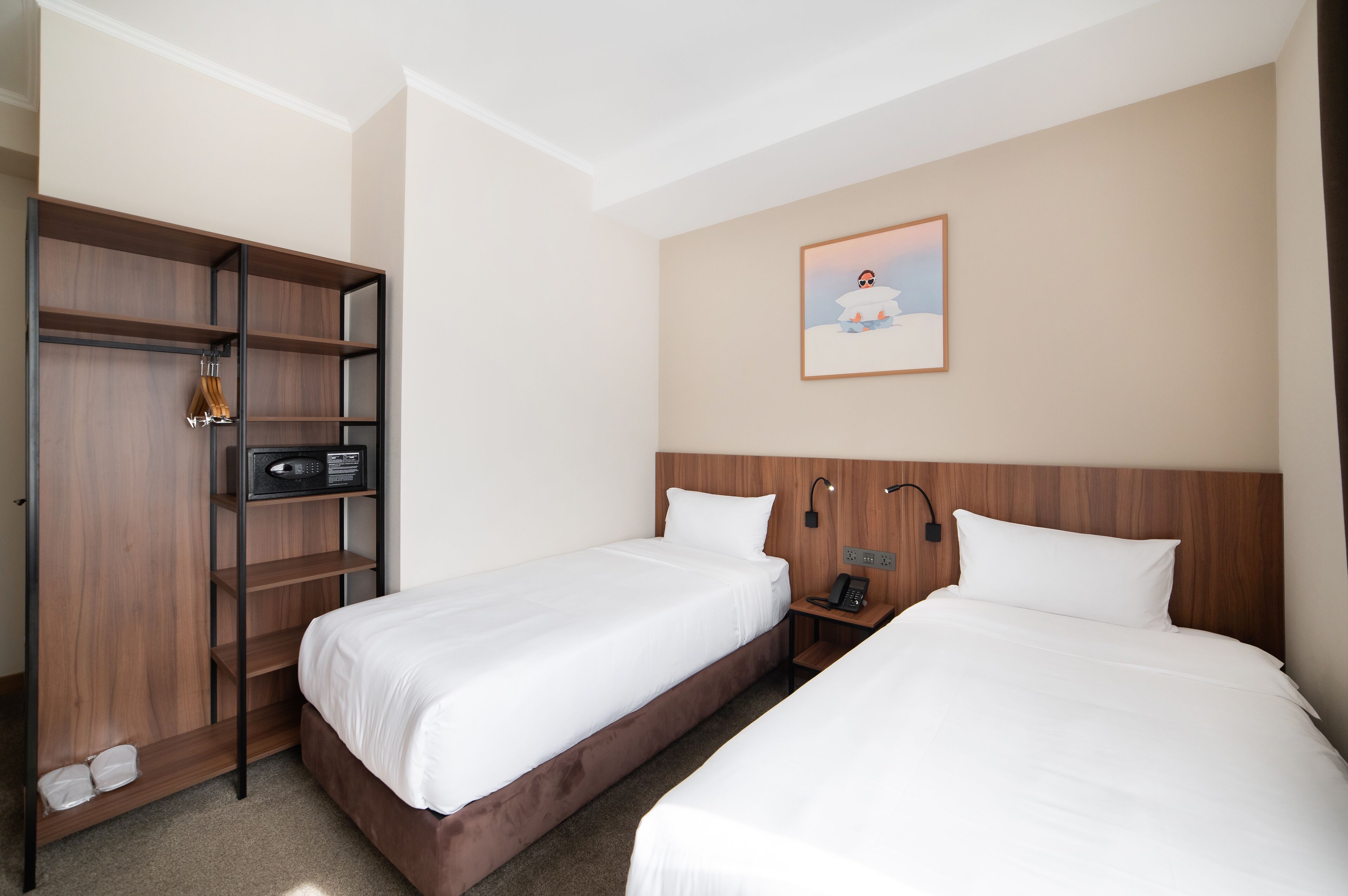 A hotel room with two beds, a wardrobe, a microwave, a phone, and a painting on the wall.