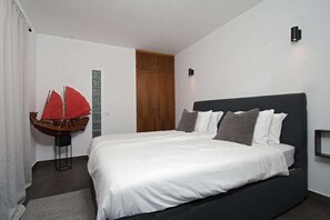 A bedroom with a bed, a wooden wardrobe, a small table with a red sailboat model, and a wall-mounted light fixture. - Comfy Apt. w/ View – Lagos (Lagos)