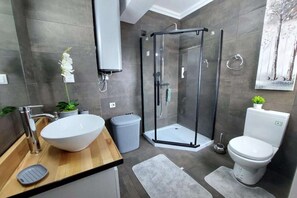 Et moderne badeværelse med en stor, hvid vask, et bruseafsnit i glas og et toilet.