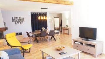 A modern living room with a TV, sofa, dining table, and chairs.